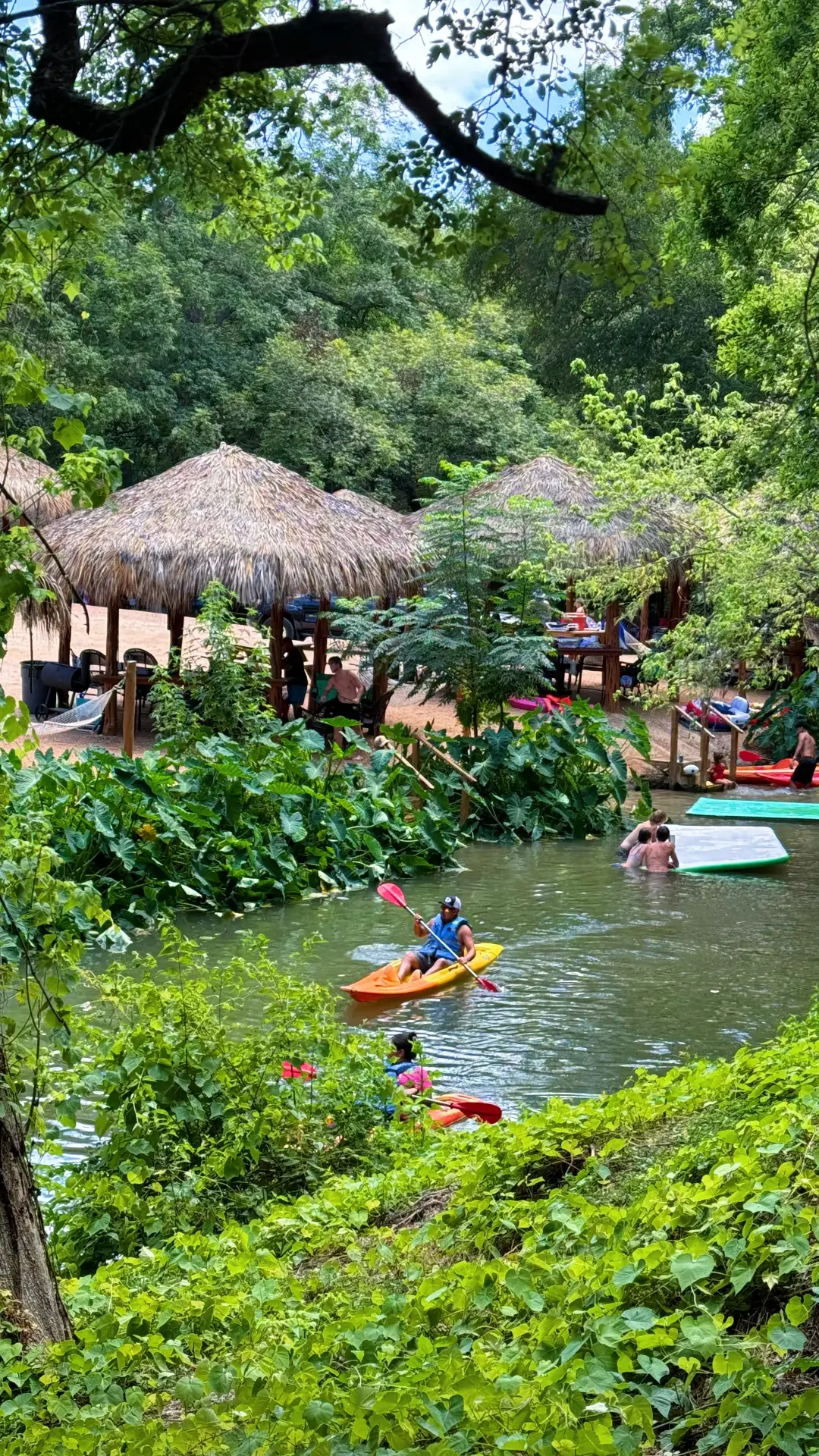 Man kayaking near San Antonio past creekside cabanas